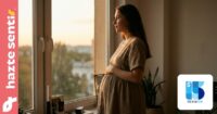 Mujer embarazada mirando por una ventana con expresión reflexiva, luz cálida de atardecer