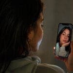 Joven mirando su reflejo en la pantalla del celular, símbolo de la banalización del cuerpo en redes sociales