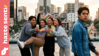 Grupo de jóvenes posando exageradamente para redes sociales mientras un joven camina en sentido contrario.